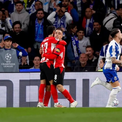 Sergiño Dest in een PSV-shirt loopt weg terwijl twee FC Porto-spelers elkaar omhelzen tijdens een Champions League-wedstrijd.