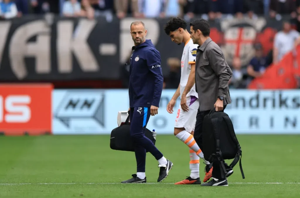 PSV-trainer Peter Bosz loopt langs de zijlijn naast een speler en een staflid op het veld.