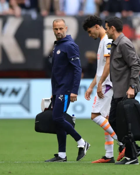 PSV-trainer Peter Bosz loopt langs de zijlijn naast een speler en een staflid op het veld.