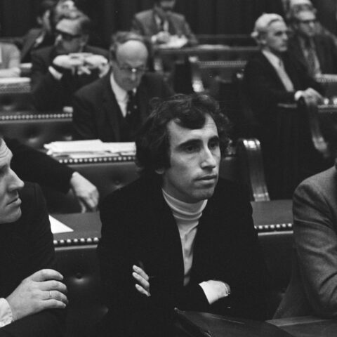Zwart-witfoto van een parlementaire zaal met meerdere mannen in pakken op banken en stoelen.