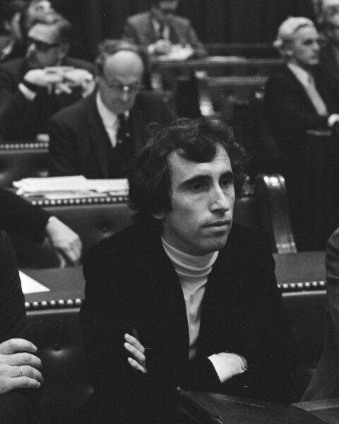 Zwart-witfoto van een parlementaire zaal met meerdere mannen in pakken op banken en stoelen.