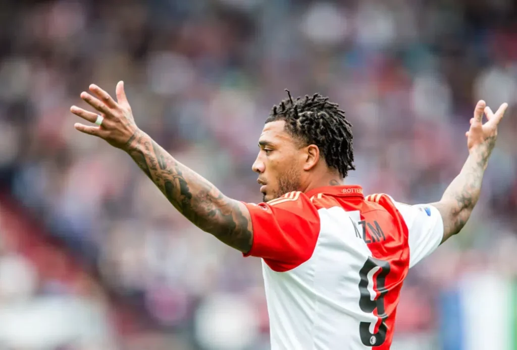 Voetballer in rood-wit shirt met gespreide armen op het veld.