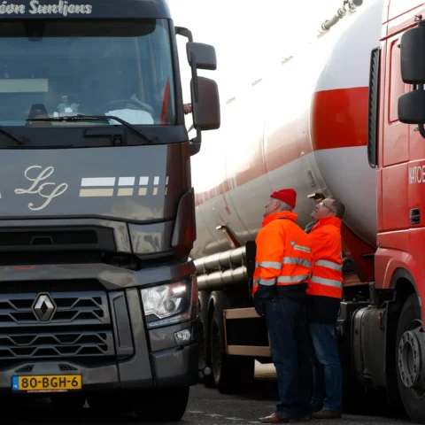 Twee vrachtwagens staan naast elkaar terwijl twee mannen in oranje veiligheidsjassen tussen de voertuigen staan.