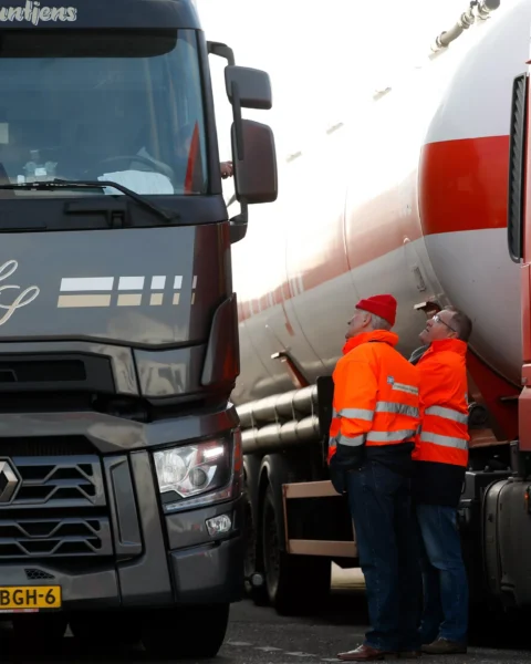Twee vrachtwagens staan naast elkaar terwijl twee mannen in oranje veiligheidsjassen tussen de voertuigen staan.