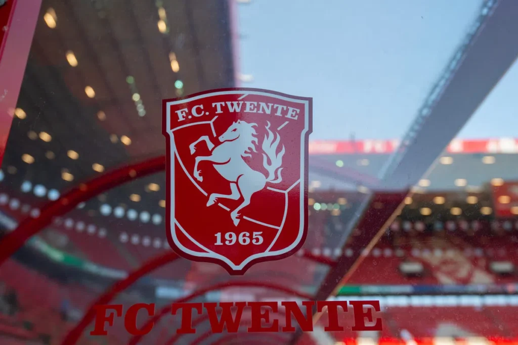 Het logo van FC Twente op een raam met stadion op de achtergrond.