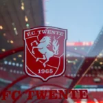 Het logo van FC Twente op een raam met stadion op de achtergrond.