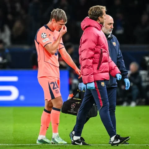 Dani Olmo staan op het veld terwijl hij zijn gezicht aanraakt, met Barcelona-staf naast hem.