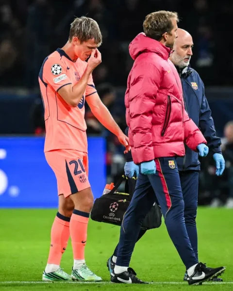 Dani Olmo staan op het veld terwijl hij zijn gezicht aanraakt, met Barcelona-staf naast hem.