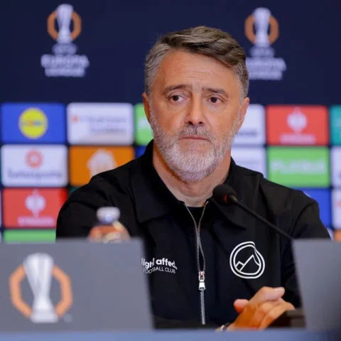 Een man zit achter een microfoon tijdens een Europa League-persconferentie.