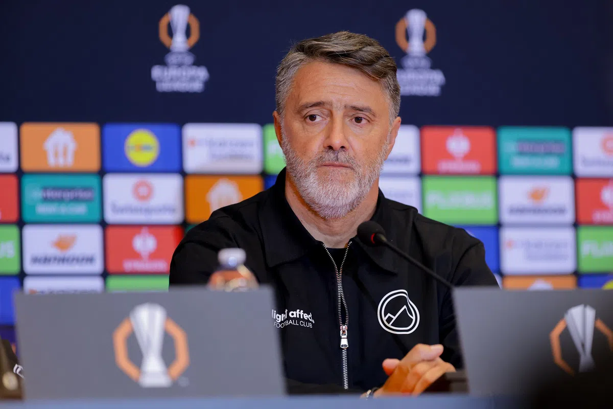 Een man zit achter een microfoon tijdens een Europa League-persconferentie.