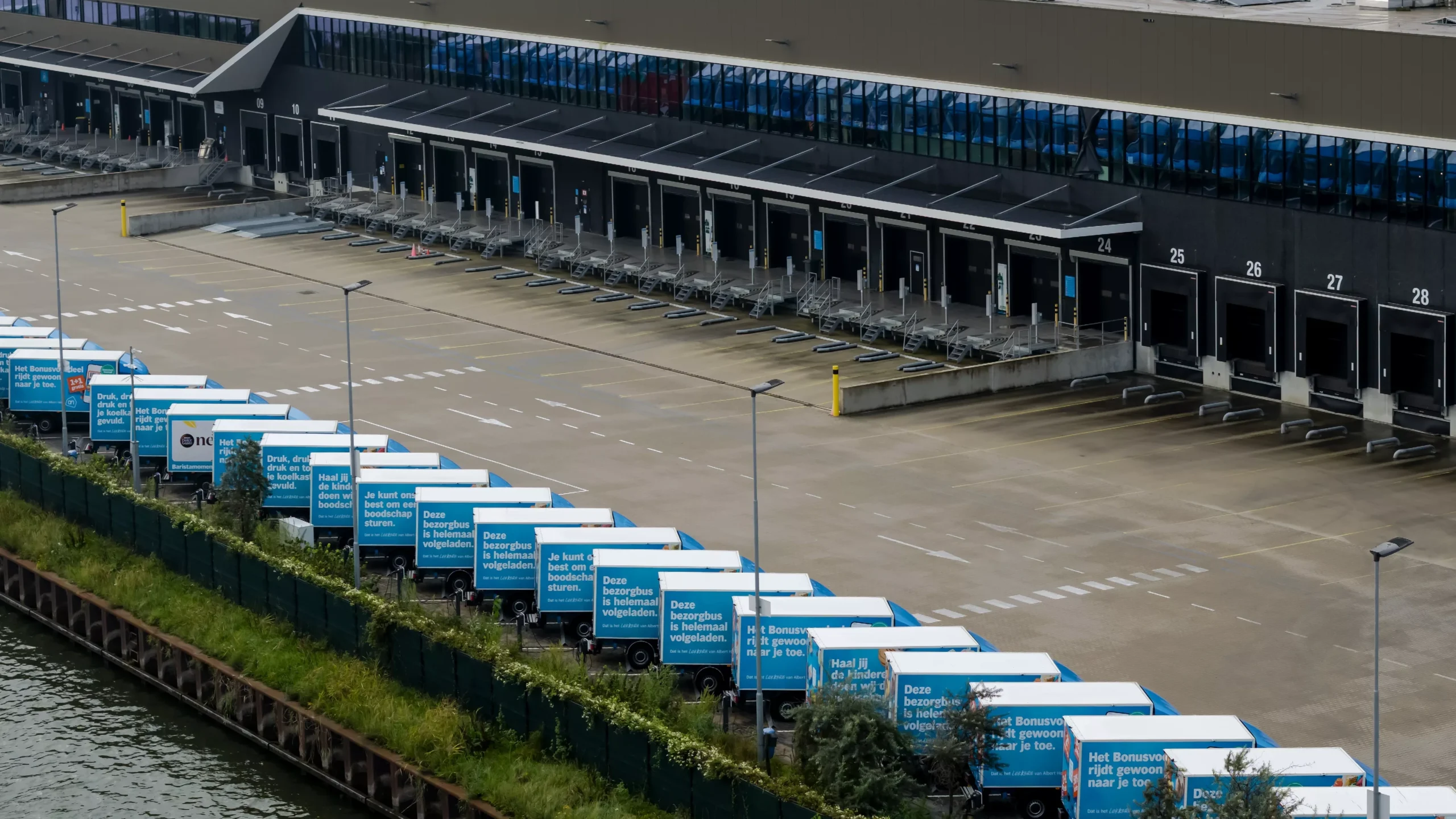 Albert Heijn-bezorgwagens staan geparkeerd bij een distributiecentrum met laadperrons.