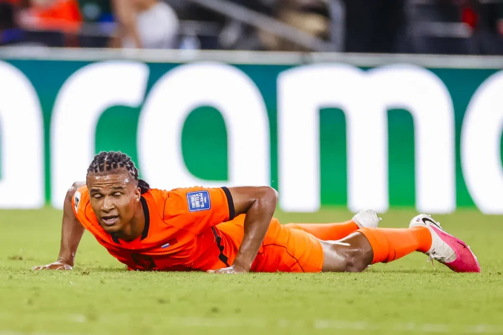 Nathan Aké ligt op het veld in een oranje voetbaltenue tijdens een wedstrijd.