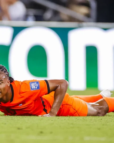 Nathan Aké ligt op het veld in een oranje voetbaltenue tijdens een wedstrijd.