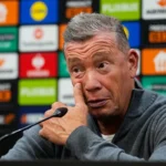 Leeroy Echteld spreekt op een persconferentie voor een sponsorachtergrond.