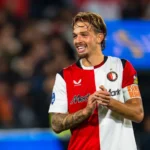 Feyenoord-speler in rood-wit shirt op het veld, glimlachend na een moment in de wedstrijd.