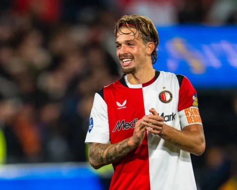 Feyenoord-speler in rood-wit shirt op het veld, glimlachend na een moment in de wedstrijd.