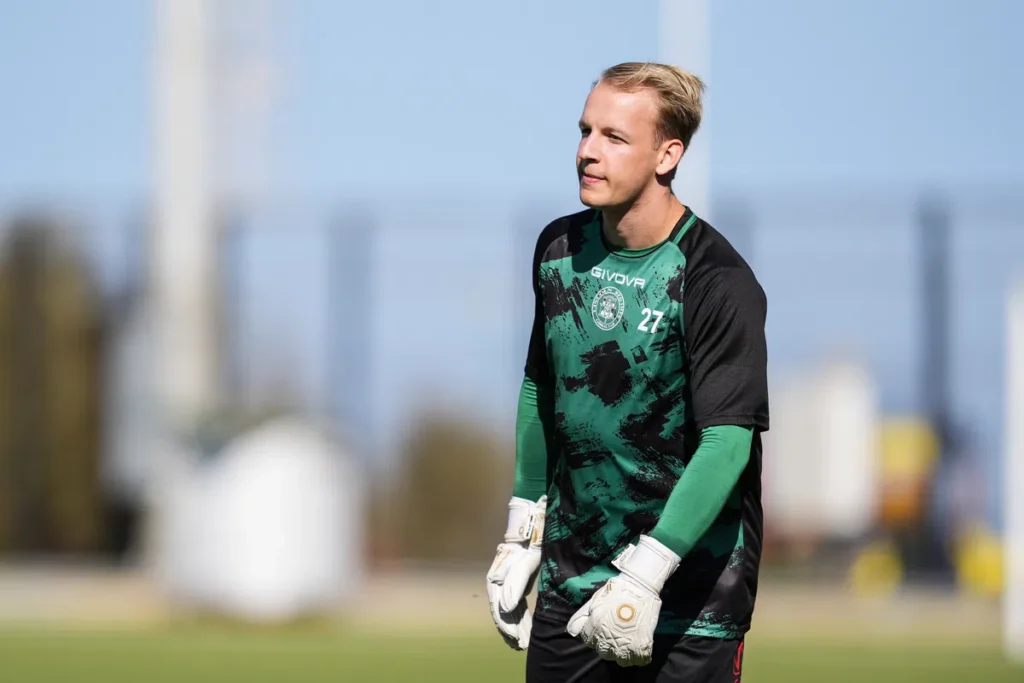 Keeper in groen-zwart tenue op een voetbalveld.