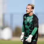 Keeper in groen-zwart tenue op een voetbalveld.