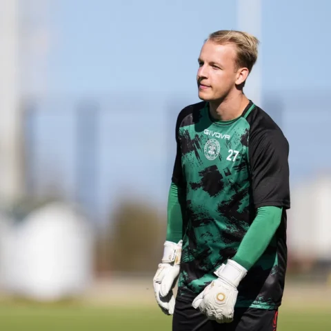 Keeper in groen-zwart tenue op een voetbalveld.