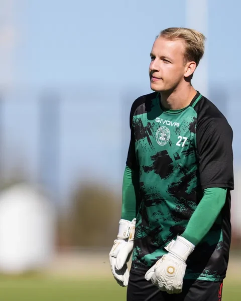 Keeper in groen-zwart tenue op een voetbalveld.